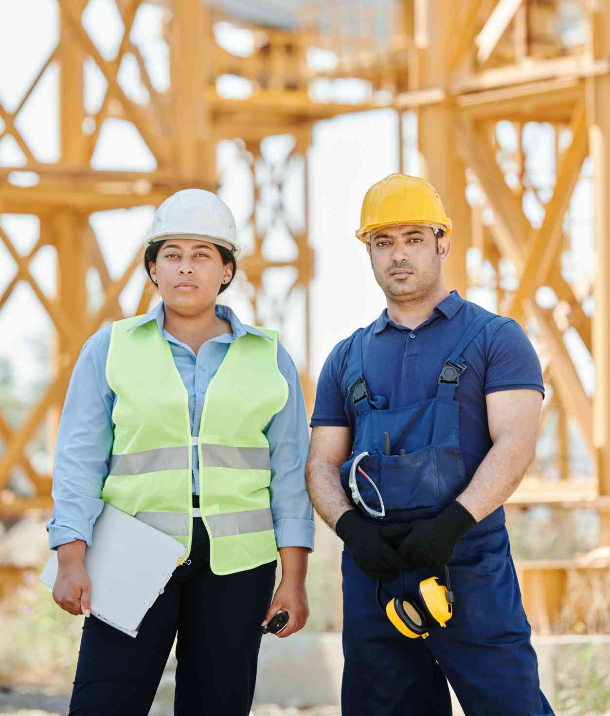 Two people in hard hats and safety vests standing next to a wooden structure.