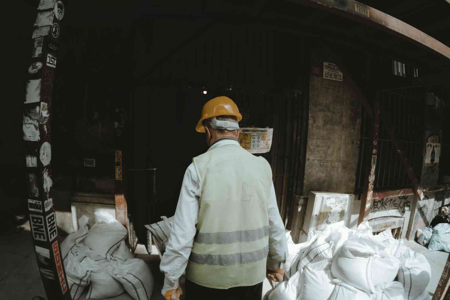 A man in a hard hat and vest walking through some bags.